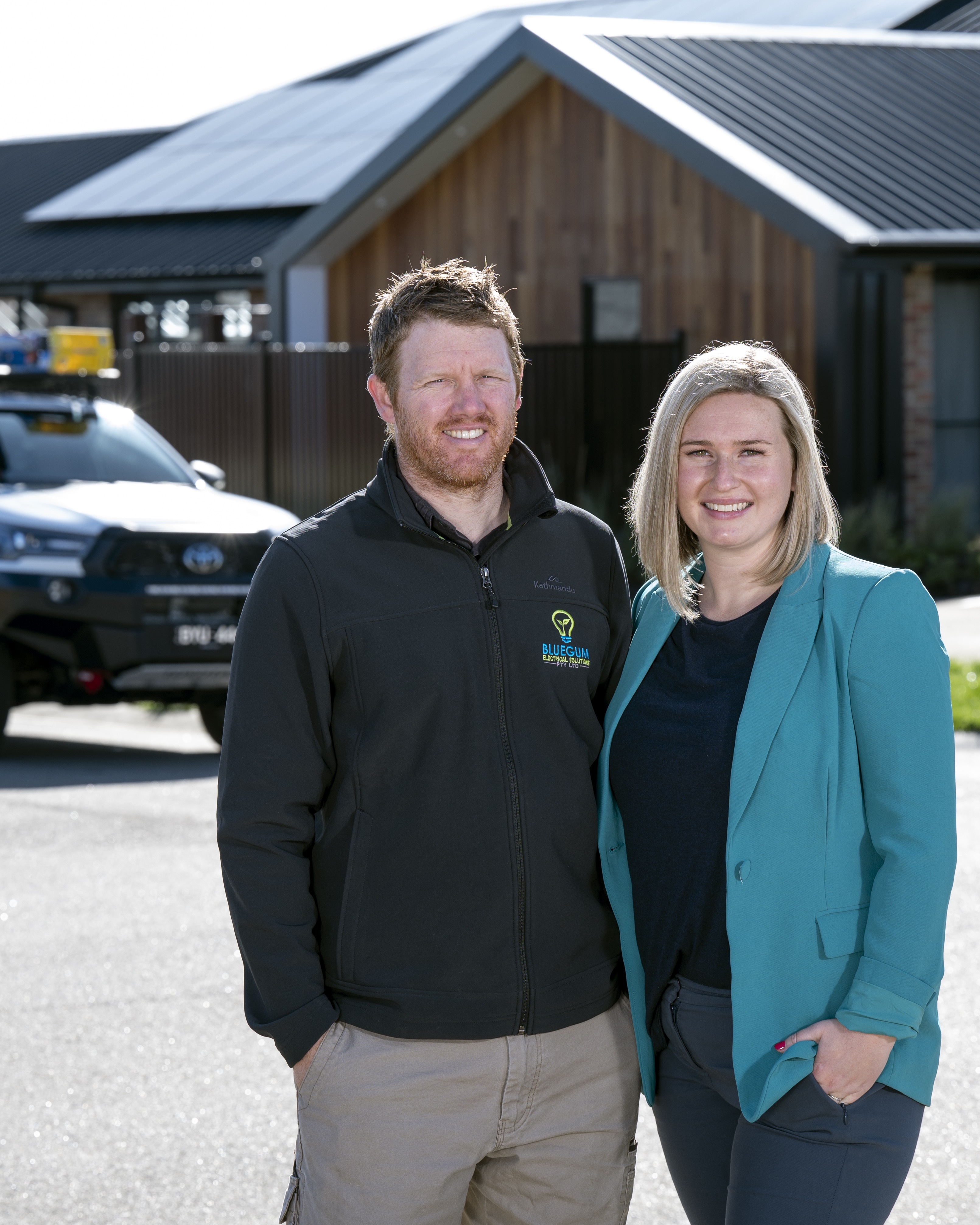 Chantel Gilbert and Josh standing in front of a Bluegum-branded ute and a Macedon Ranges home with rooftop solar
